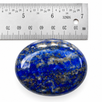 Polished blue Lapis Lazuli palm stone beside a metal ruler showing its size