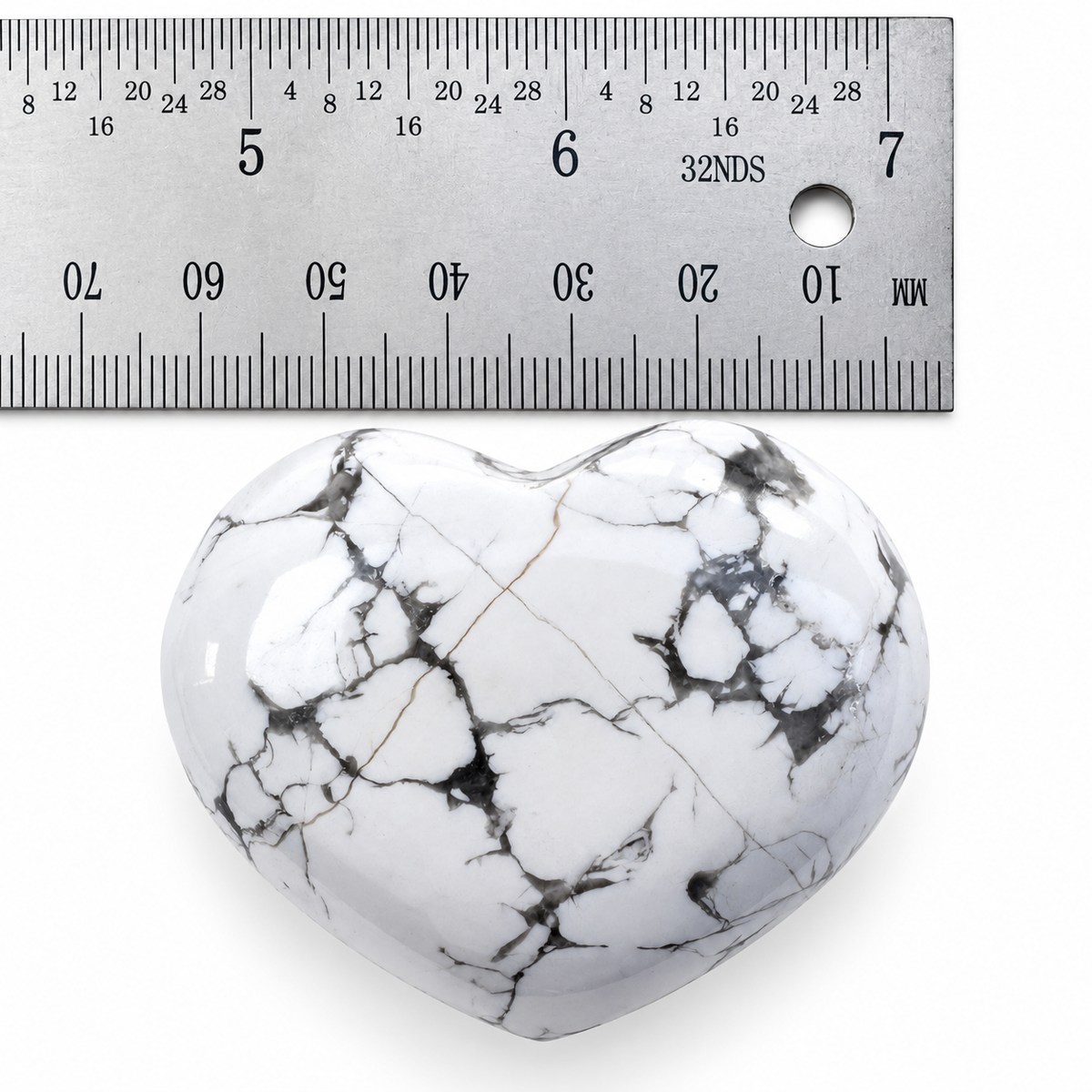 White Howlite heart palm stone with grey marbling beside metal ruler