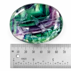 Green and purple Rainbow Fluorite palm stone beside metal ruler for size reference